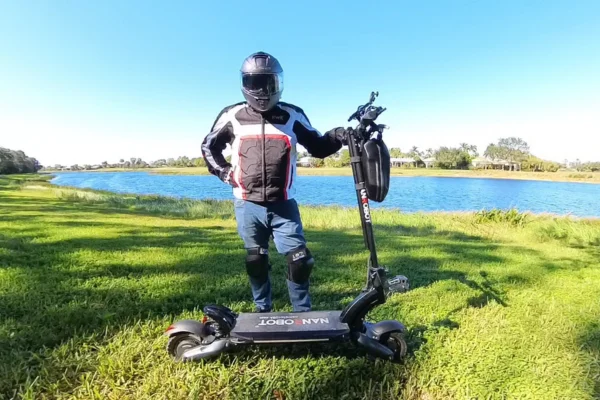 Hobart standing with electric scooter in the grass by a lake.